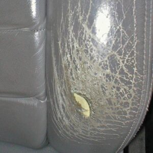 Damaged leather seat bolster with cracks and hole before repair