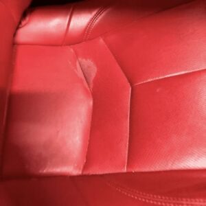 Discolored red leather car seat with a faded patch caused by a cleaning product